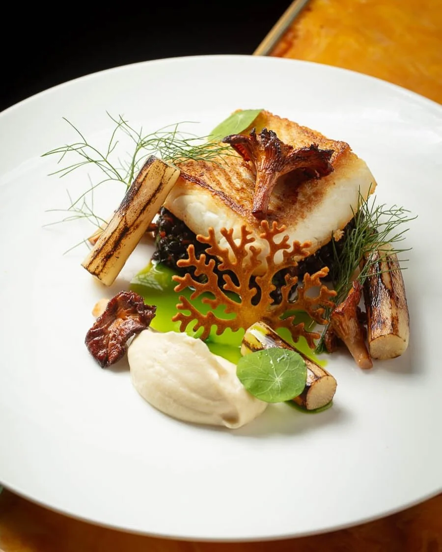 A golden fish portion with vegetables and a pale purée